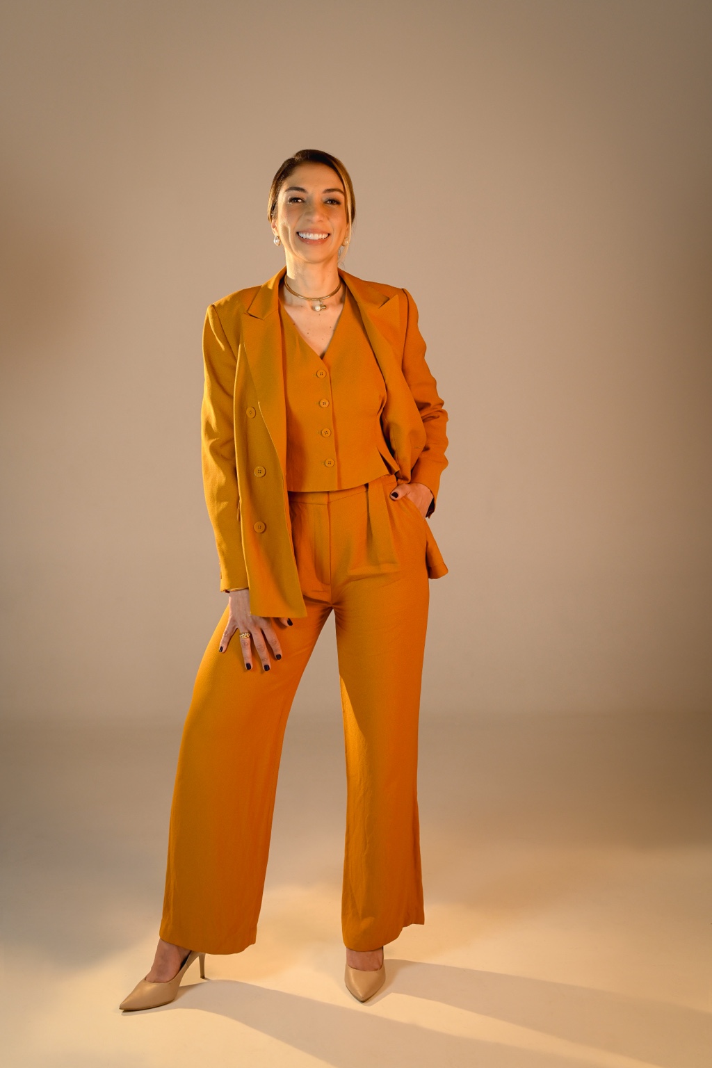 Carla Modesto em retrato profissional, com conjunto de alfaiataria mostarda.