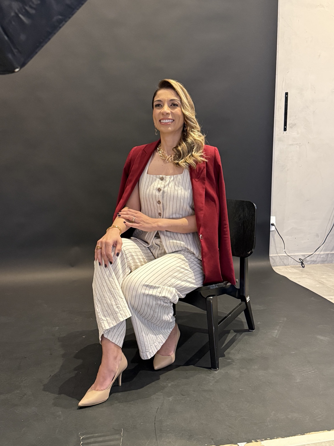 Carla Modesto sentada, com blazer bordô sobre os ombros.